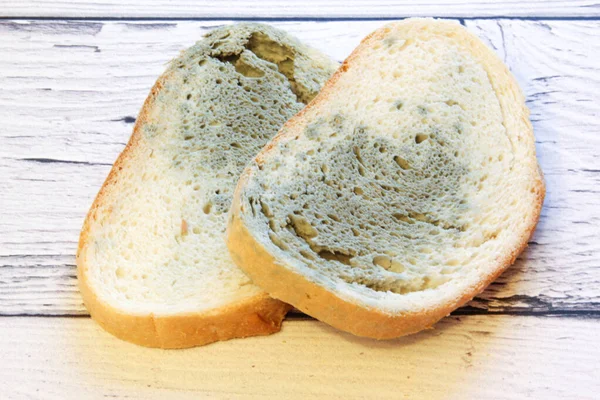 Schimmel wächst schnell auf schimmeligem Brot auf Holzboden. Mehltau auf einer Scheibe Brot. Altes Brot, mit Mehltau bedeckt. — Stockfoto