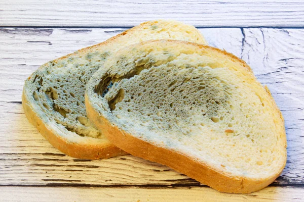 Schimmel wächst schnell auf schimmeligem Brot auf Holzboden. Mehltau auf einer Scheibe Brot. Altes Brot, mit Mehltau bedeckt. — Stockfoto