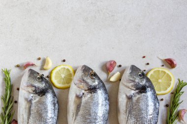 Gri bir zemin üzerinde baharat ve limon bulunan üç taze, organik deniz dorado 'su. Uzayı kopyala Üst görünüm