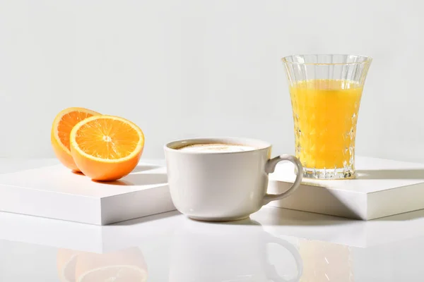 view of a cup of freshly made coffee between an orange cut in half and a glass of orange juice on a table on a light background. Fruit and coffee concept.