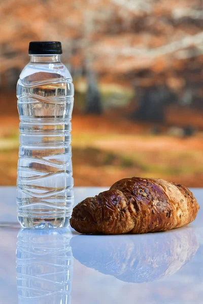 Primer Plano Una Botella Agua Junto Delicioso Croissant Una Mesa — Foto de Stock