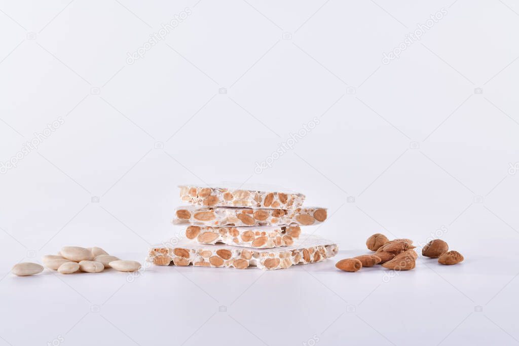 Delicious looking blocks of almond nougat surrounded by peeled and unpeeled almonds on alight background. Traditional sweets and abstract concept.