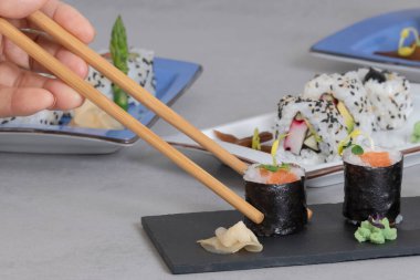 Yemek çubuklarını kapatın ve etrafı suşiyle çevrili tepsiden lezzetli bir maki toplayın. Suşi ve sağlıklı gıda konsepti.