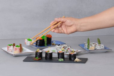 Bir kadın elinin yemek çubuklarıyla lezzetli maki ve uramaki parçalarının bir karışımından uramaki parçalarını topladığı seçici bir odak noktası..