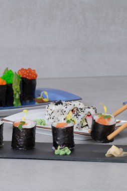 Yemek çubuklarıyla tepsilerde maki ve uramaki karışımından bir parça alın. Suşi ve sağlıklı gıda konsepti.