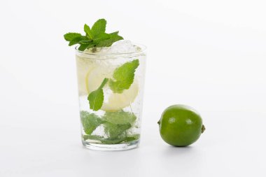 Serinletici bir bardak mojito kokteyli, arka planda taze bir limonun yanında.