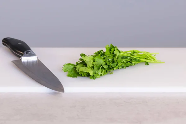 Close up of parsley next to a kitchen knife in a cutting board on an out of focus background — Stock Photo, Image