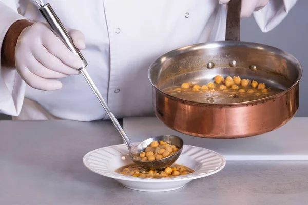 Uitzicht op kikkererwtenstoofpot wordt geserveerd door een mannelijke chef-kok met behulp van een lepel op een out of focus achtergrond — Stockfoto