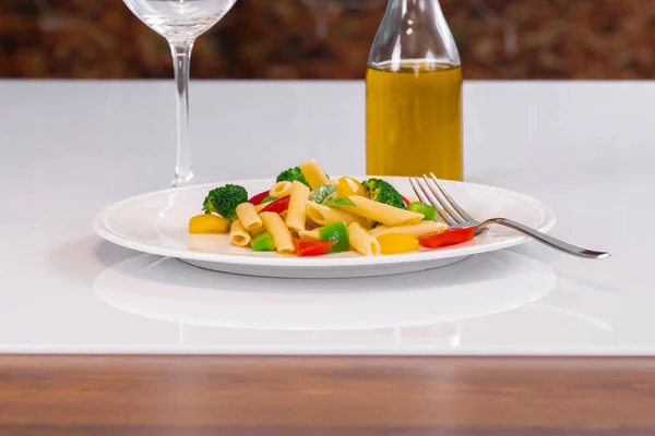 Селективный фокус тарелки с салатом из макарон и вилкой, с нефокусированной бутылкой масла в задней части. Концепция пасты и здорового питания. — стоковое фото
