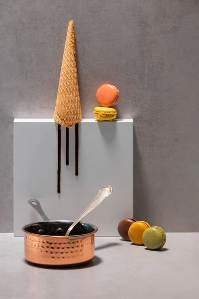 Вид на каструлю з ложкою біля різноманітних макарунів з порожнім конусом морозива — стокове фото