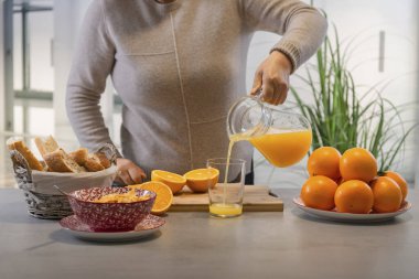 Bardağa taze portakal suyu döken bir kadın.