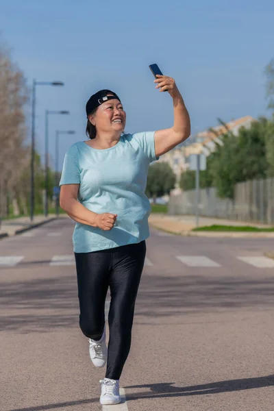 Азиатская женщина бежит и улыбается на свой телефон — стоковое фото