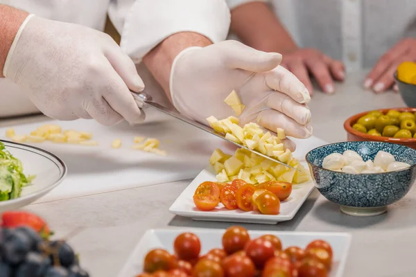 Cuoco di sesso maschile che indossa guanti mettendo mele tagliate su un piatto con il coltello: focus selettivo — Foto Stock