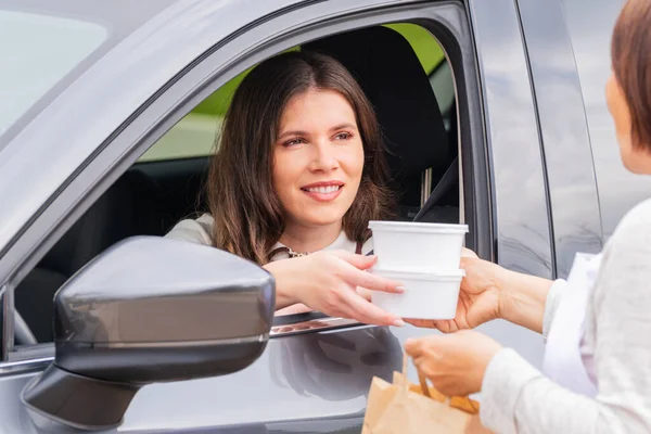 Mulher em um carro agarrando takeaway recipientes de comida — Fotografia de Stock