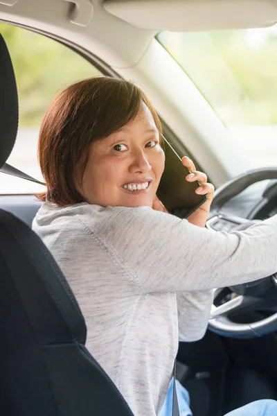 Зрелая азиатка в машине разговаривает по телефону — стоковое фото