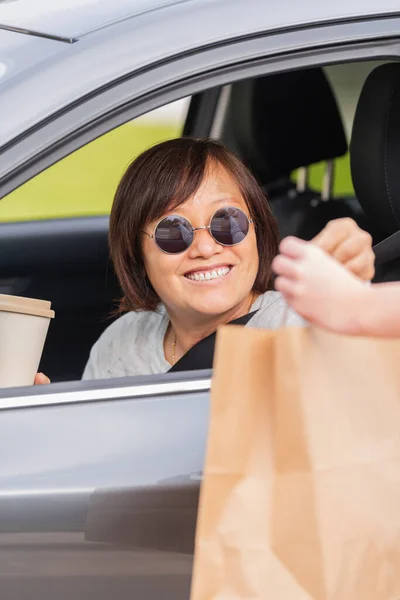 Sorrindo maduro asiático mulher em um carro trocando um saco de papel — Fotografia de Stock