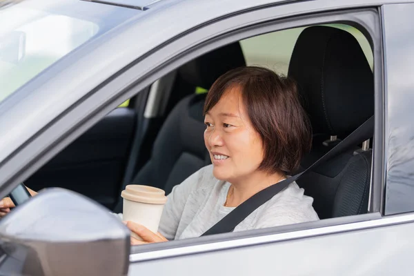 Uma mulher asiática madura em um carro segurando uma xícara de papel: foco seletivo. Conceito de estilo de vida. — Fotografia de Stock