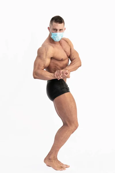 Vit man bär en kirurgisk mask gör bodybuilding pose: Selektivt fokus. Fitness och covid 19 konceptet — Stockfoto