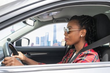 Afro-Amerikalı kadın araba kullanırken mutlu bir şekilde gülümsüyor: Seçici odak ve yan çekim.