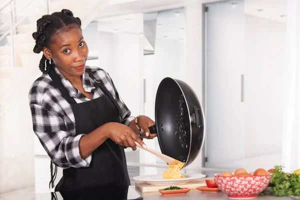 Smiling afro american woman moving scrambled eggs into a plate — Stock Photo, Image