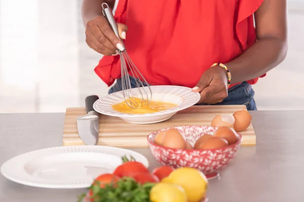 Primo piano della donna afro-americana con una frusta su alcune uova: concetto di cucina — Foto Stock