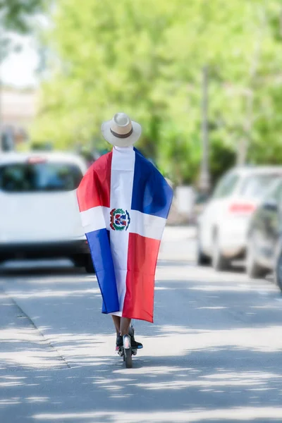 Dominikai Köztársaság zászló csomagolt latin férfi lovaglás egy elektromos robogó az utcán — Stock Fotó