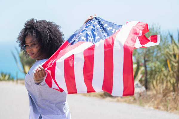 Afro american girl waving an american flag on a road