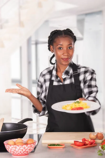 Afro amerikai nő köténnyel, finom rántottát kínál a kamerának. — Stock Fotó