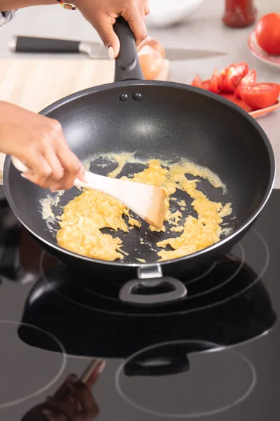 Close up female afro american hands stirring eggs on a deep frying pan — Stock Photo, Image