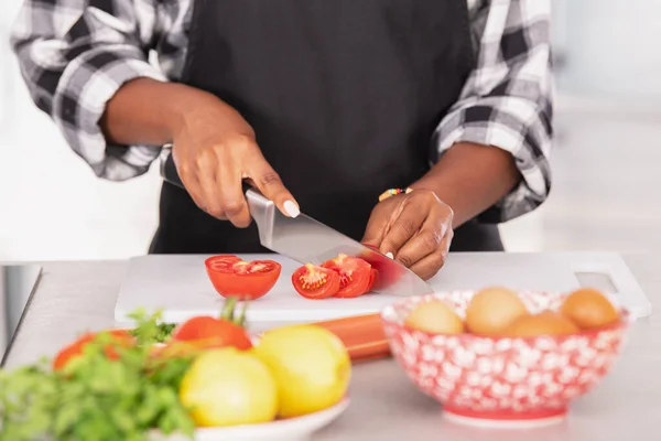 Afroamerykanka umiejętnie kroi pomidory na desce do krojenia — Zdjęcie stockowe