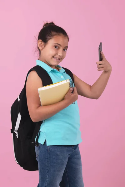 Schulmädchen hält ein Notizbuch und macht ein Selfie mit Blick in die Kamera — Stockfoto