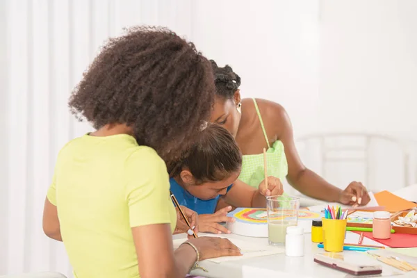 Side view of a little girl painting with her two teachers in art class