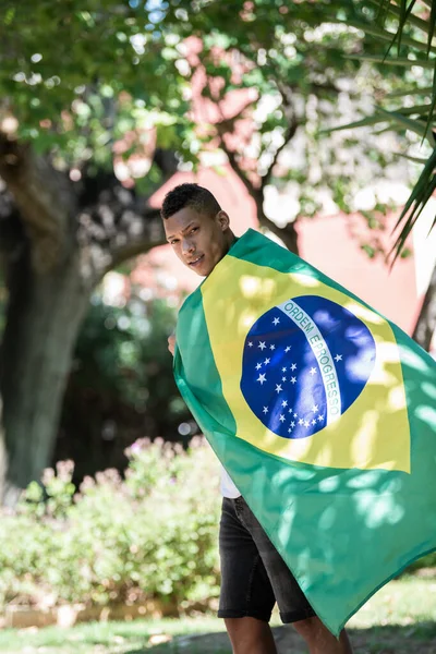 A brazil zászlóba csomagolt latin férfi a kamerába néz: szelektív fókusz. A sokszínűség fogalma. — Stock Fotó