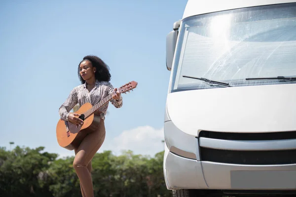 Młoda kobieta stojąca na gitarze na świeżym powietrzu z vanem obok niej — Zdjęcie stockowe