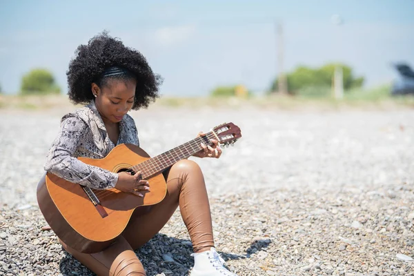 Młoda kobieta siedząca na żwirowej kamiennej ziemi w powietrzu opery grająca na gitarze — Zdjęcie stockowe