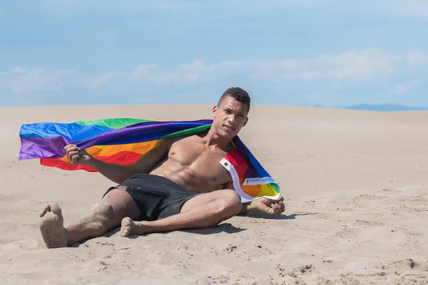 Obekymrad man med en gay stolthet flagga när du ligger på stranden. — Stockfoto