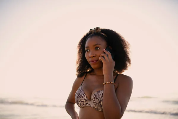 在阳光明媚的海滩上拿着手机聊天的年轻女人 — 图库照片