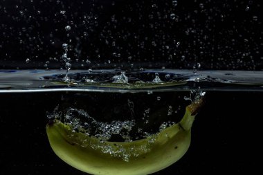 Siyah arka planda suya düşen renkli sarı muzun yakın görüntüsü.