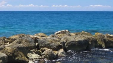 Dalgaların taşların üzerinde kırılışının muhteşem görüntüsü. Atlantik Okyanusu 'nun turkuaz suyu ve mavi arka planda büyük kayalar. Ağır çekim. Willemstad. Curacao.