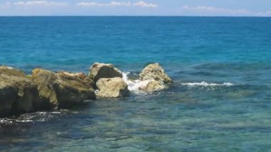 Dalgaların taşların üzerinde kırılışının muhteşem görüntüsü. Atlantik Okyanusu 'nun turkuaz suyu ve mavi arka planda büyük kayalar. Ağır çekim. Willemstad. Curacao.