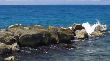 Ağır çekim. Dalgaların taşların üzerinde kırılışının muhteşem görüntüsü. Atlantik Okyanusu 'nun turkuaz suyu ve mavi arka planda büyük kayalar. Willemstad. Curacao.