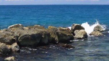 Taşlarda kırılan dalgaların güzel manzarası. Atlantik Okyanusu 'nun turkuaz suyu ve mavi arka planda büyük kayalar. Ağır çekim. Willemstad. Curacao.