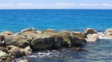 Ağır çekim. Dalgaların taşların üzerinde kırılışının muhteşem görüntüsü. Atlantik Okyanusu 'nun turkuaz suyu ve mavi arka planda büyük kayalar. Willemstad. Curacao.