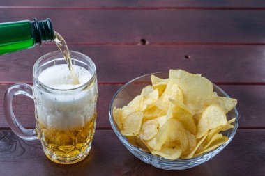 Bardağa ve patates cipsine dökülen biranın yakın görüntüsü.