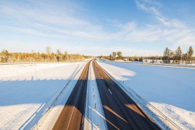 Kış otobanı üzerinde güzel bir manzara. Aydınlık kış gününde kar ve mavi gökyüzüyle kaplı yan tarlalar. Güzel bir doğa geçmişi var. İsveç.