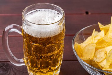 Biranın cam bardak ve bir fincan patates cipsi içindeki görüntüsünü kapat..