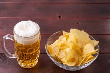 Biranın cam bardak ve bir fincan patates cipsi içindeki görüntüsünü kapat..