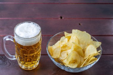 Biranın cam bardak ve bir fincan patates cipsi içindeki görüntüsünü kapat..