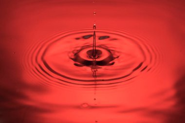 Kırmızıda izole edilmiş mavi su yüzeyinde daireler çizen damlaların yakın görüntüsü.