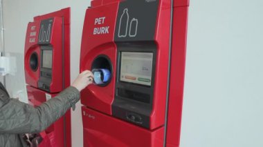 Kadının otomatik geri dönüşüm makinesine plastik şişe koyuşunu yakından izle. Avrupa. İsveç. Uppsala. 04.30.2021.